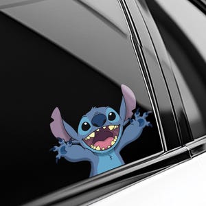 May include: A blue cartoon character sticker with large ears, a wide grin, and outstretched arms. The sticker is applied to a car window, with the character's face and arms visible. The background is a dark, reflective surface.