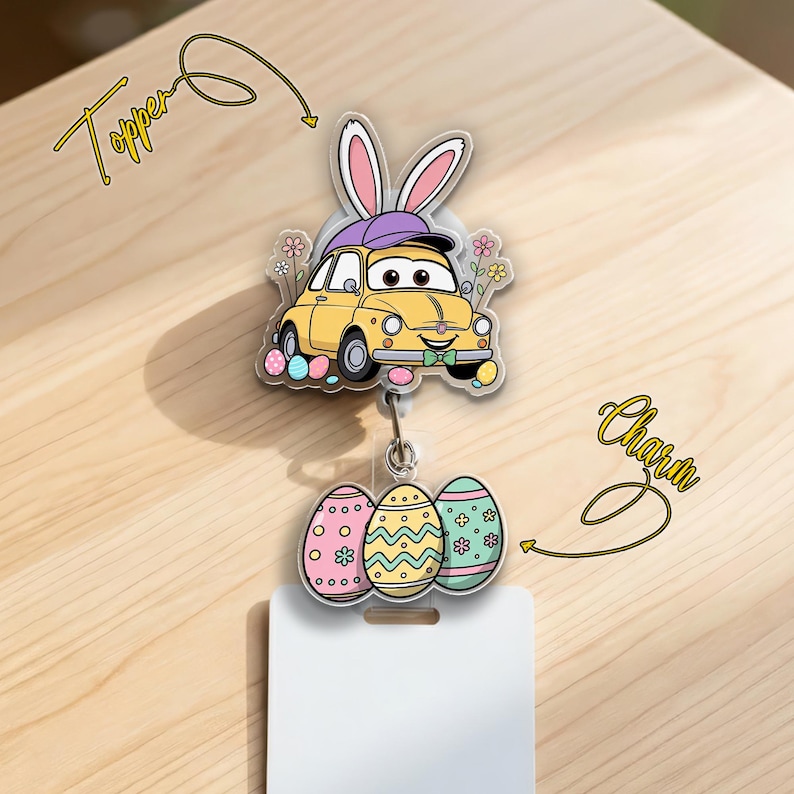 May include: A yellow car-shaped badge reel topper with bunny ears and a purple hat, paired with a charm of three decorated Easter eggs. The topper and charm are attached to a white badge holder.