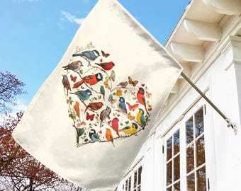 May include: A white flag with a heart-shaped design featuring a variety of colorful birds. The birds are arranged in a heart shape and are surrounded by green leaves and flowers.