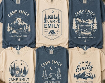 May include: Six t-shirts in blue and cream colors, each featuring a unique graphic print with the text Camp Emily Lake Tahoe 2026. The designs include illustrations of mountains, pine trees, tents, a canoe, a lantern, and a campfire.