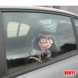 May include: A vinyl car sticker featuring the character Edna Mode from The Incredibles. Edna is shown with her iconic round glasses, bob haircut, and a stern expression. The sticker is applied to a car window.