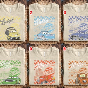 May include: Six beige t-shirts with different Cars movie character designs. Each shirt features a character's name, a checkered flag design, and the text "Rusteze 2006". Characters include Luigi, Sally, Doc, Chick Hicks, Mack, and Mater.