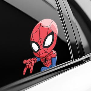 Pode incluir: Um autocolante vermelho e azul do Homem-Aranha, com a m&aacute;scara e o fato do super-her&oacute;i. O autocolante parece estar a espreitar por uma janela de carro, com uma m&atilde;o a apontar. O design &eacute; em estilo cartoon.