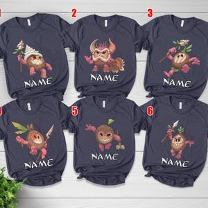 Puede incluir: Camisetas azul marino con personajes de coco de dibujos animados. Cada camiseta presenta un dise&ntilde;o de personaje diferente con una cara sonriente, sosteniendo varios objetos. La palabra "NAME" est&aacute; impresa debajo de cada personaje.