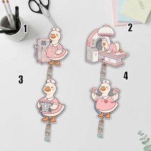 May include: Four acrylic badge reels featuring a cartoon duck dressed as a nurse. The duck is wearing a pink uniform and cap. Each reel depicts the duck in a different medical scenario, including using medical equipment and holding x-rays.