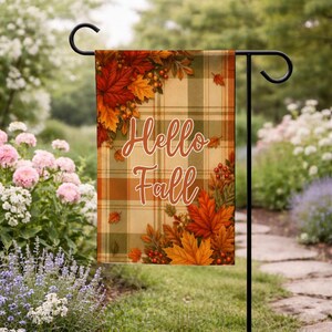 May include: A rectangular garden flag featuring a beige and green plaid background with the text Hello Fall in white script. The design is decorated with clusters of orange, red, and yellow autumn maple leaves and small red berries in the corners.