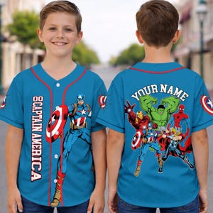 May include: A light blue baseball jersey featuring Captain America and other Marvel superheroes. The jersey has red trim and the words "CAPTAIN AMERICA" printed vertically on the front. The back of the jersey has the words "YOUR NAME" above a group of superheroes.