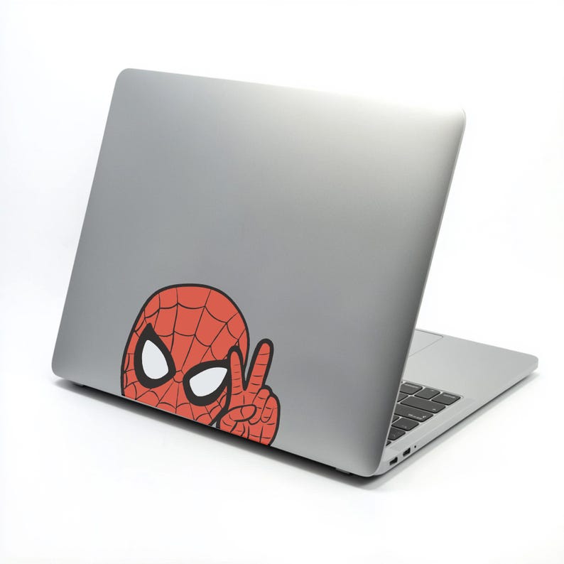 Pu&ograve; includere: Un laptop argentato con un adesivo di Spider-Man rosso e nero sul retro. L'adesivo mostra la maschera di Spider-Man con occhi bianchi e una mano che fa il segno della pace.