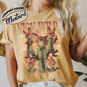 May include: A mustard yellow t-shirt featuring a graphic print of the character Nick Wilde in various poses. The design includes the text NICK WILDE in a retro font, surrounded by red lightning bolts and sparkles on a vintage-style cotton fabric.