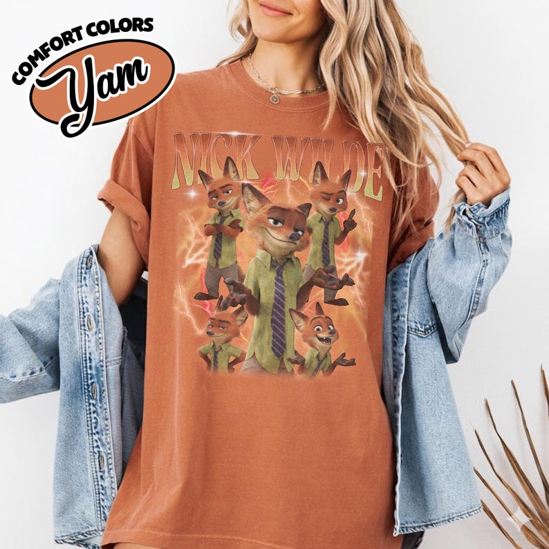 May include: A rust-colored short-sleeve t-shirt featuring a graphic print of the character Nick Wilde in various poses. The text "NICK WILDE" appears in a light green font above the character, set against a background of orange lightning bolts.