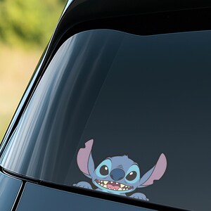 Puede incluir: Una calcoman&iacute;a de vinilo azul y morada del personaje Stitch de la pel&iacute;cula de Disney Lilo & Stitch. La calcoman&iacute;a est&aacute; aplicada a la ventana de un coche, con Stitch asomando por la parte inferior. La calcoman&iacute;a tiene un estilo de dibujos animados.