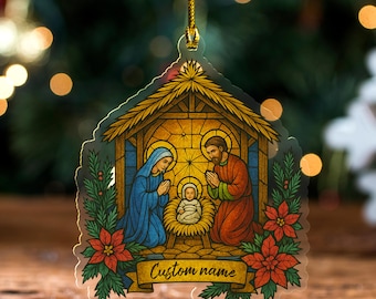 May include: A Christmas ornament featuring a Nativity scene with Mary, Joseph, and baby Jesus. The ornament has a gold string for hanging and includes the text "Custom name" on a banner. Red poinsettias and green leaves frame the bottom.