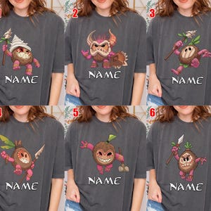 Puede incluir: Seis camisetas grises, cada una con un dise&ntilde;o &uacute;nico de personaje de dibujos animados. Los personajes son criaturas parecidas a cocos con varios accesorios y expresiones. Cada camiseta tiene la palabra "NAME" impresa debajo del personaje.