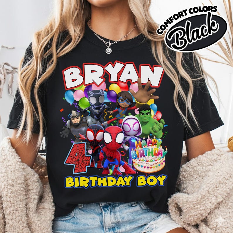 May include: A black t-shirt featuring a graphic print of various superhero characters, a colorful birthday cake, and the text "BRYAN", "4", and "BIRTHDAY BOY". The design includes balloons and confetti, with a "COMFORT COLORS Black" label in the corner.