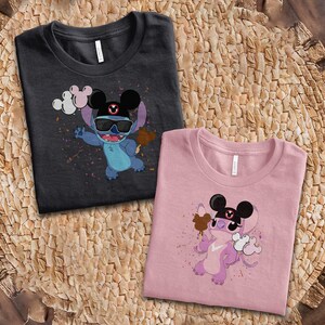 K&ouml;nnte beinhalten: Zwei T-Shirts mit einer Zeichentrickfigur, die eine Sonnenbrille und einen Mickey-Mouse-Hut tr&auml;gt. Eines der Shirts ist dunkelgrau, das andere rosa. Die Figur h&auml;lt ein braunes Eis und Luftballons. Die Shirts liegen auf einer gewebten Oberfl&auml;che.