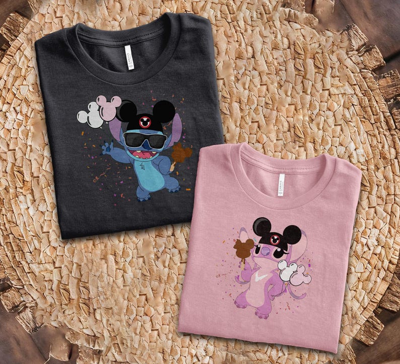 K&ouml;nnte beinhalten: Zwei T-Shirts mit einer Zeichentrickfigur, die eine Sonnenbrille und einen Mickey-Mouse-Hut tr&auml;gt. Eines der Shirts ist dunkelgrau, das andere rosa. Die Figur h&auml;lt ein braunes Eis und Luftballons. Die Shirts liegen auf einer gewebten Oberfl&auml;che.