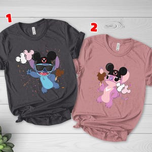 K&ouml;nnte beinhalten: Zwei T-Shirts, eines in Anthrazit und eines in Staubrosa, jeweils mit einer Cartoonfigur, die eine Sonnenbrille und einen Mickey-Mouse-Hut tr&auml;gt. Die blaue Figur h&auml;lt ein Eis und Luftballons, w&auml;hrend die lila Figur ein Eis und Luftballons h&auml;lt.