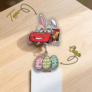 May include: A red car-shaped badge reel topper with bunny ears and sunglasses, paired with a charm of three decorated Easter eggs. The topper and charm are connected to a white badge holder. The word "Topper" and "Charm" are written in cursive.