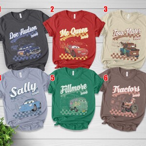 May include: Six short-sleeve t-shirts in charcoal, red, beige, light blue, green, and brown. Each shirt features a character from the movie Cars, including Doc Hudson, Mc Queen, Tow Mater, Sally, Fillmore, and Tractors, with the year 2006 printed.