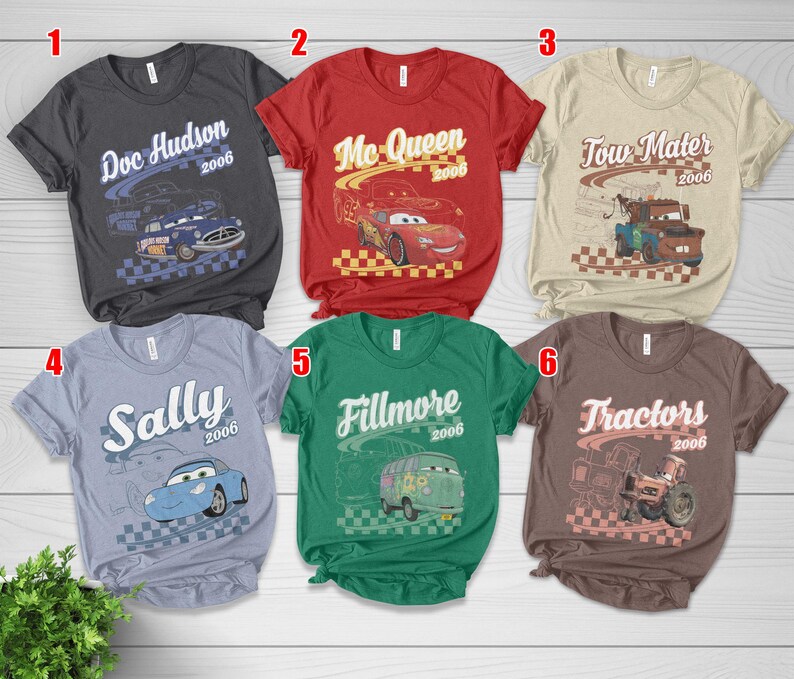 May include: Six short-sleeve t-shirts in charcoal, red, beige, light blue, green, and brown. Each shirt features a character from the movie Cars, including Doc Hudson, Mc Queen, Tow Mater, Sally, Fillmore, and Tractors, with the year 2006 printed.
