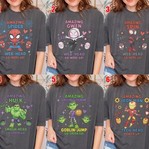 May include: Six charcoal grey t-shirts, each with a superhero design. The shirts showcase characters like Spider-Man, Gwen, and Iron Man, accompanied by phrases such as "Web-Head" and "Tech-Head," along with related illustrations.