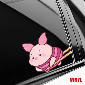 May include: A pink Piglet vinyl sticker with a striped shirt, appearing to be stuck in a car window. The sticker has a cartoon design with the word "VINYL" in red.