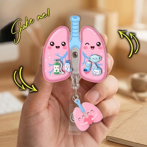 May include: A badge reel featuring a large, pink, cartoon-style lung shape with a light blue trachea. The lungs contain small, floating medical icons and a smaller, dangling lung charm. The text "Shake me!" is written in yellow cursive script.