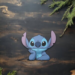 May include: A blue cartoon character with large black eyes, large ears, and a thoughtful expression. The character is resting its chin on its hand. The background is a dark wood surface with green sprigs.