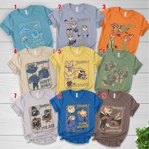 Pode incluir: Nove camisetas coloridas com personagens do filme "Zootopia 2". Cada camisa exibe um personagem ou grupo de personagens diferente com seus nomes. As camisas s&atilde;o de v&aacute;rias cores, incluindo azul, laranja, amarelo e cinza.
