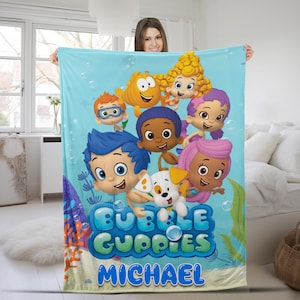 May include: A light blue fleece blanket featuring the Bubble Guppies characters and their puppy, Bubble Puppy, with the text Bubble Guppies and the name Michael printed in blue letters against an underwater scene with bubbles and coral.