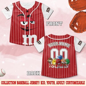 Puede incluir: Camiseta de b&eacute;isbol roja y blanca con rayas verticales y la cara del personaje de M&M's en la parte delantera. La parte trasera presenta el texto "YOUR NAME" encima del n&uacute;mero "00" y un grupo de personajes de M&M's. Mangas blancas con el logo de M&M's.