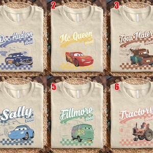 May include: A collection of six beige t-shirts featuring Disney Pixar Cars characters. Each shirt displays a character name, the year 2006, a checkered pattern, and a graphic of Doc Hudson, Mc Queen, Tow Mater, Sally, Fillmore, or Tractors.