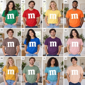 May include: A collection of twelve short-sleeve crew neck t-shirts in various solid colors, each featuring a large white lowercase letter m printed on the center of the chest. The shirts are displayed in a grid of twelve individual images.