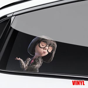 May include: A white ceramic mug with a black handle and the text "But First, Coffee" in a bold, black font. The mug is set against a blurred background. The mug appears to be approximately 10 cm tall.