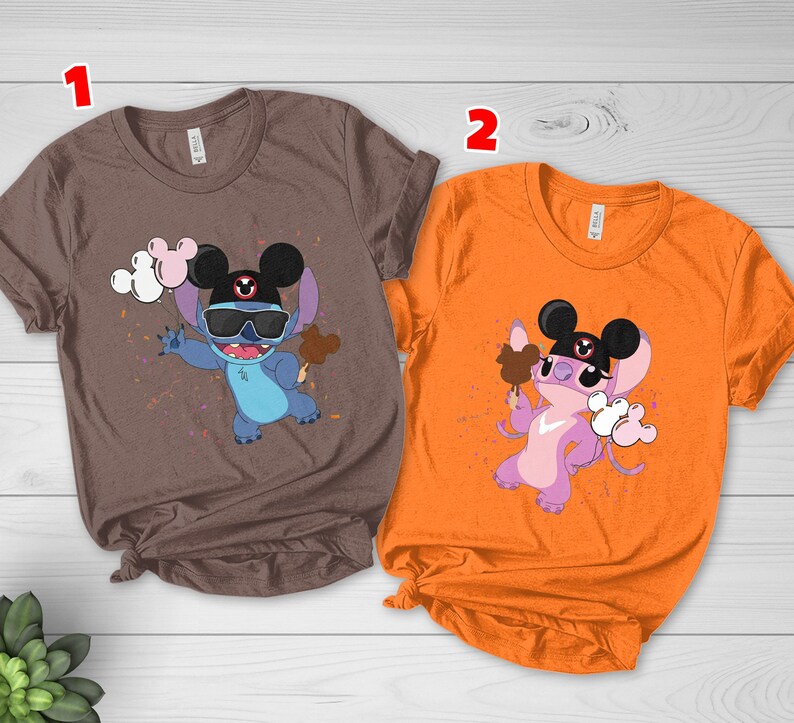 K&ouml;nnte beinhalten: Zwei T-Shirts, eines braun und eines orangefarben, mit einer Cartoonfigur, die eine Sonnenbrille und einen Mickey Mouse-Hut tr&auml;gt. Die Figur h&auml;lt ein Eis und Luftballons. Die T-Shirts sind kurz&auml;rmlig.