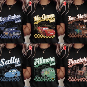May include: A black t-shirt featuring six different character designs from the movie Cars. Each design includes the character name, the year 2006, a line art sketch, a colored illustration of the vehicle, and a checkered flag pattern at the bottom.