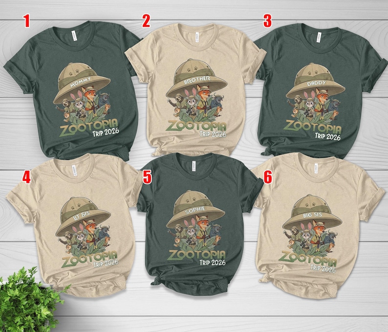 May include: Six short-sleeved t-shirts in different colours, each with a Zootopia cartoon graphic. The shirts display family member names on safari hats, with the text "ZOOTOPIA TRIP 2026" beneath the graphic.