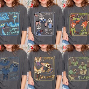 Pode incluir: Seis camisetas cinza escuro com personagens do filme de anima&ccedil;&atilde;o "Zootopia 2". Cada camisa tem um design diferente com personagens como Gary de Snake, Judy Hopps, Nick Wilde, Chief Bogo, Finnick e Flash, com seus nomes.