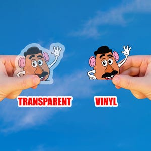 Peut inclure: Deux autocollants repr&eacute;sentant un personnage de dessin anim&eacute; avec une t&ecirc;te marron, une moustache noire et un chapeau noir. Un autocollant est transparent et l'autre est en vinyle. Le mot "TRANSPARENT" est dans un encadr&eacute; rouge et le mot "VINYL" est dans un encadr&eacute; rouge.