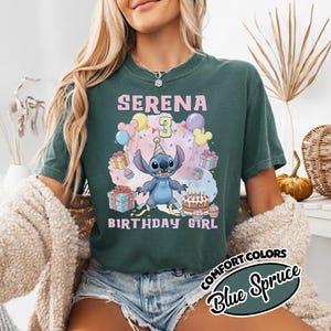 Peut inclure: Un t-shirt vert fonc&eacute; avec un motif du personnage Stitch portant un chapeau de f&ecirc;te, entour&eacute; de ballons, de cadeaux et d'un g&acirc;teau d'anniversaire. Le texte indique SERENA 3 BIRTHDAY GIRL en lettres roses. Le t-shirt a un col rond.