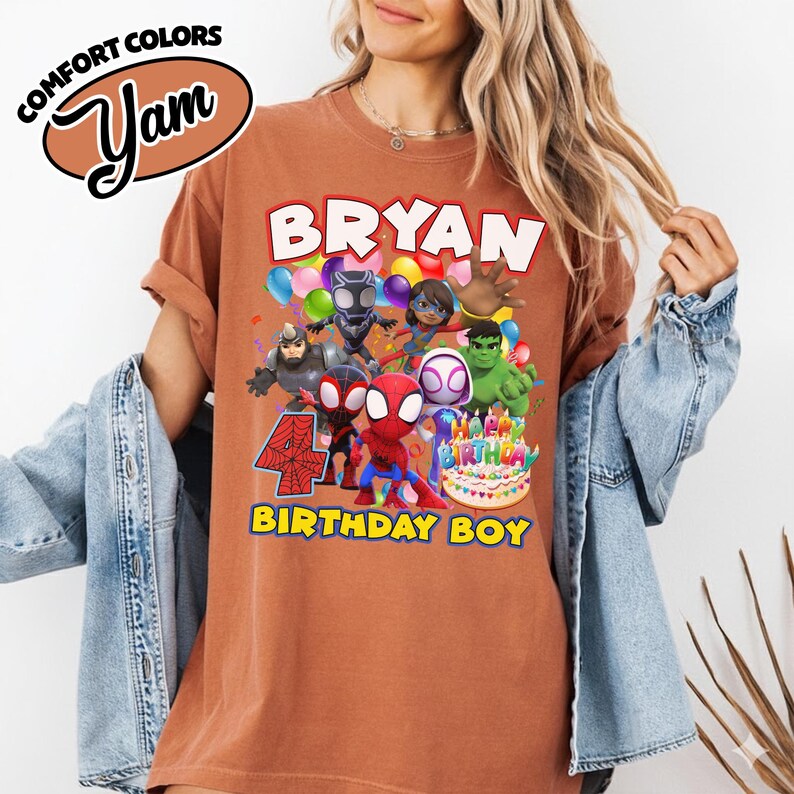 May include: A rust-colored t-shirt featuring a graphic print of various superhero characters, a birthday cake, and the text "BRYAN", "4", and "BIRTHDAY BOY". The shirt has a crew neckline and short sleeves, with a "COMFORT COLORS" logo in the corner.