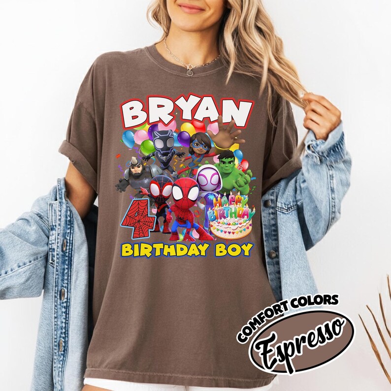 May include: A brown short-sleeve t-shirt featuring a graphic print of various superhero characters, a birthday cake, and the text BRYAN, 4, and BIRTHDAY BOY. The shirt is layered under a blue denim jacket. The color is labeled as Comfort Colors Espresso.