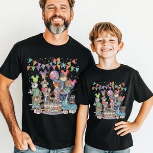 May include: Black t-shirts with a colorful birthday graphic. The graphic features cartoon animals, a cake, balloons, and the number 4. The shirts are worn by a man and a child.