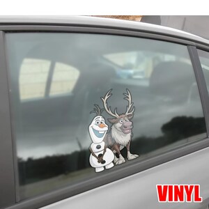 Puede incluir: Una calcoman&iacute;a de vinilo con los personajes Olaf el mu&ntilde;eco de nieve y Sven el reno de la pel&iacute;cula animada Frozen. La calcoman&iacute;a est&aacute; aplicada a la ventana de un coche. La palabra "VINYL" est&aacute; impresa en rojo.