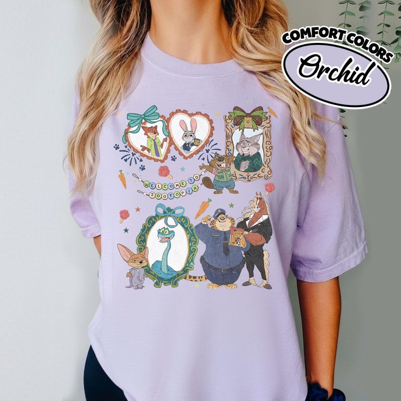 May include: A light purple short-sleeve t-shirt featuring a graphic print of various animated animal characters from Zootopia. The design includes framed portraits, a banner with the text Welcome to Zootopia, carrots, and popsicles.