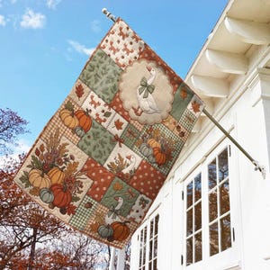Pu&ograve; includere: Una bandiera rettangolare da esterno con un design patchwork a tema autunnale, che include oche bianche con fiocchi verdi, zucche arancioni e verdi, ghiande marroni e foglie autunnali nei toni dell'arancione, del marrone e del verde.