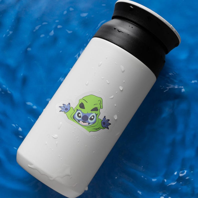 May include: White insulated tumbler with a black lid. A green and blue cartoon character sticker is on the side. The tumbler is on a blue surface with water droplets.