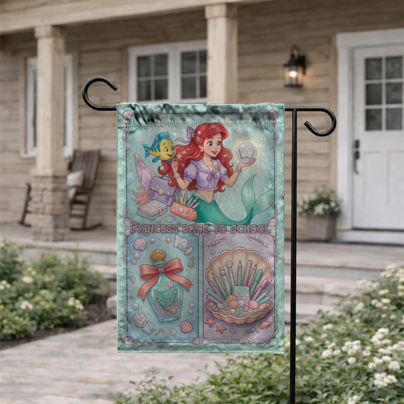 Puede incluir: Una bandera de jard&iacute;n turquesa con Ariel de La Sirenita y Flounder. La bandera tiene el texto "PRINCESS BACK TO SCHOOL" e incluye ilustraciones de &uacute;tiles escolares y una concha con brochas de maquillaje.