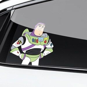 K&ouml;nnte beinhalten: Ein farbenfroher Vinyl-Aufkleber von Buzz Lightyear aus Toy Story. Der Aufkleber zeigt die Figur in ihrem charakteristischen gr&uuml;nen, wei&szlig;en, lila und schwarzen Raumanzug mit verschr&auml;nkten Armen. Der Aufkleber ist auf einer Autoscheibe angebracht.