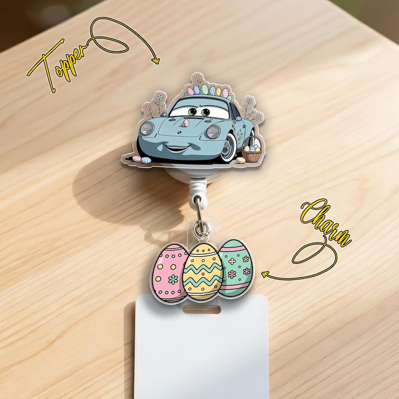 May include: A badge reel with a light blue cartoon car topper and three Easter egg charms. The car has a basket of eggs and a colorful egg on top. The charms are pink, yellow, and blue with floral and geometric designs. The reel has a white card holder.